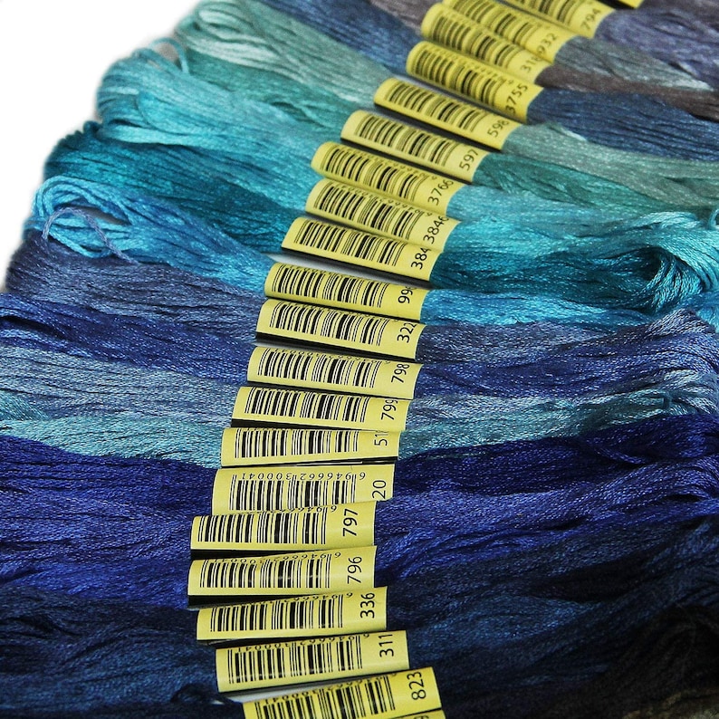 May include: A collection of 18 skeins of embroidery floss in shades of blue and teal. The floss is wound around yellow cardboard spools with barcodes and numbers printed on them. The numbers on the spools are 823, 311, 336, 796, 797, 19, 51, 799, 798, 322, 99, 384, 3846, 3766, 597, 20, 5, 3755, 318932, and 794.