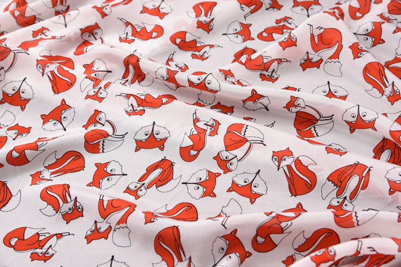 May include: White fabric with a repeating pattern of red foxes. The foxes are drawn in a simple, cartoon style and are facing different directions.