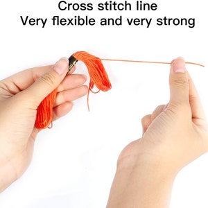 May include: Close-up of a hand holding a spool of orange embroidery floss. The floss is being pulled taut, demonstrating its flexibility and strength. The text "Cross stitch line Very flexible and very strong" is visible above the hand.