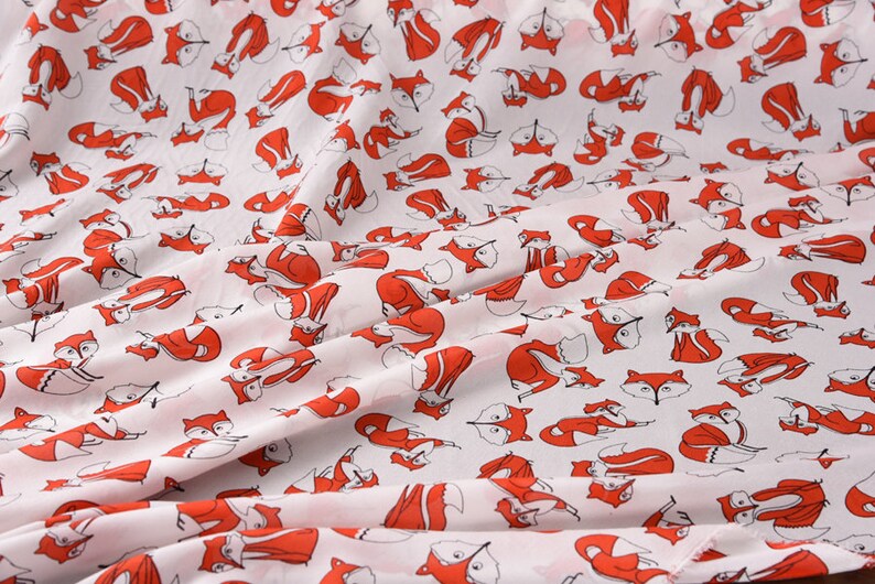 May include: White fabric with a repeating pattern of red foxes. The foxes are all facing the same direction and have black eyes and noses.