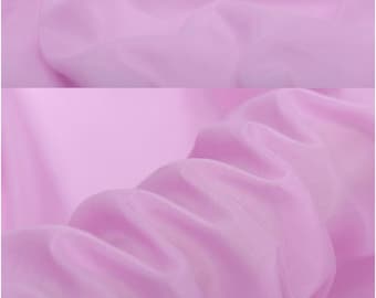 Puede incluir: Primer plano de una tela rosa claro con una textura suave y sedosa. La tela está drapeada y doblada, mostrando su naturaleza fluida y delicada.