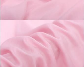 Puede incluir: Primer plano de una tela suave y rosa con una textura lisa. La tela está drapeada y doblada para mostrar su naturaleza fluida.