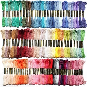 May include: A collection of 100 embroidery floss skeins in a variety of colors, including red, blue, green, yellow, orange, purple, pink, brown, and white. Each skein is wrapped in a black label with white text.