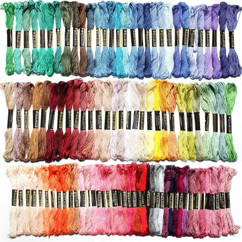 May include: A collection of 100 embroidery floss skeins in a variety of colors, including red, blue, green, yellow, orange, purple, pink, brown, and white. Each skein is wrapped in a black label with white text.