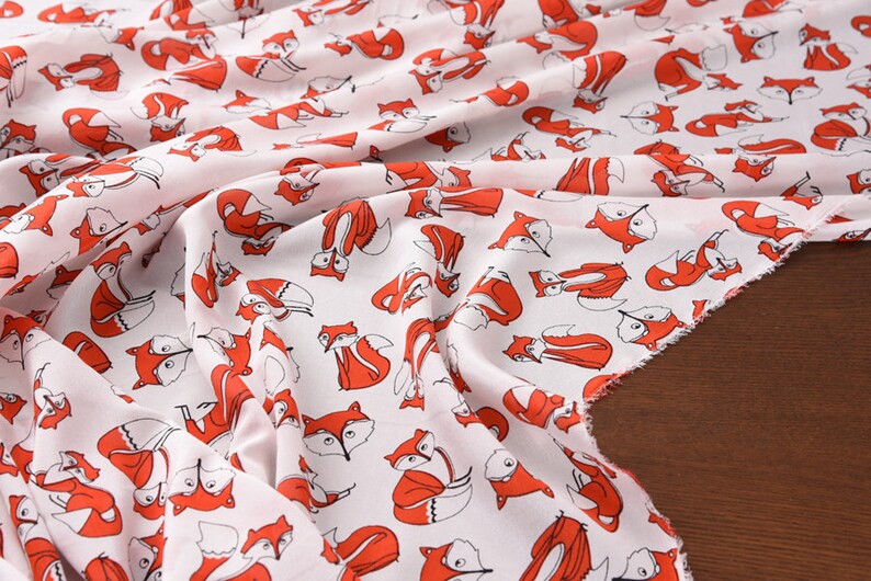 May include: White fabric with a repeating pattern of red foxes. The foxes are drawn in a simple, cartoon style.
