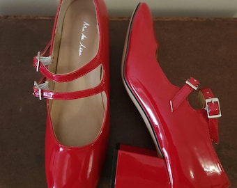 May include: A pair of red patent leather heeled shoes with double straps and buckles. The shoes have a block heel and a pointed toe.