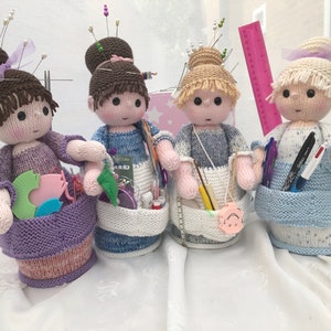 May include: Four knitted doll pincushions with different colored yarn and hair. Each doll is holding various sewing and crafting supplies in a basket.