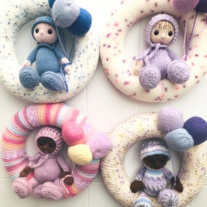 May include: Four knitted wreaths, each featuring a doll and balloons. The wreaths are white with pink and white speckles, white with pink flowers, pink and white stripes, and white with blue speckles. The dolls are wearing hats and have different skin tones. The balloons are pink, blue, and purple.