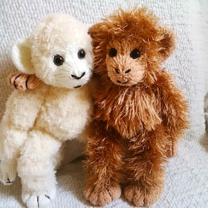 May include: A white fluffy knitted lamb toy and a brown fluffy knitted monkey toy. Both toys are sitting on a white fuzzy surface.