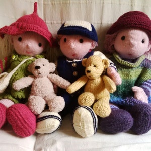 Könnte beinhalten: Drei gestrickte Puppen, zwei mit Teddybären, eine mit rotem Hut, eine mit blauem Hut und eine mit lila Hut.