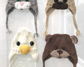 Könnte beinhalten: Vier gestrickte Mützen mit Tiergesichtern. Die Mützen sind grau, beige, weiß und braun. Jede Mütze hat eine lange, baumelnde Schleife. Die Mützen sind alle nach vorne gerichtet.