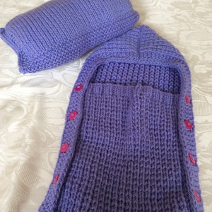 May include: A purple knitted baby sleeping bag with a hood and buttons down the side.