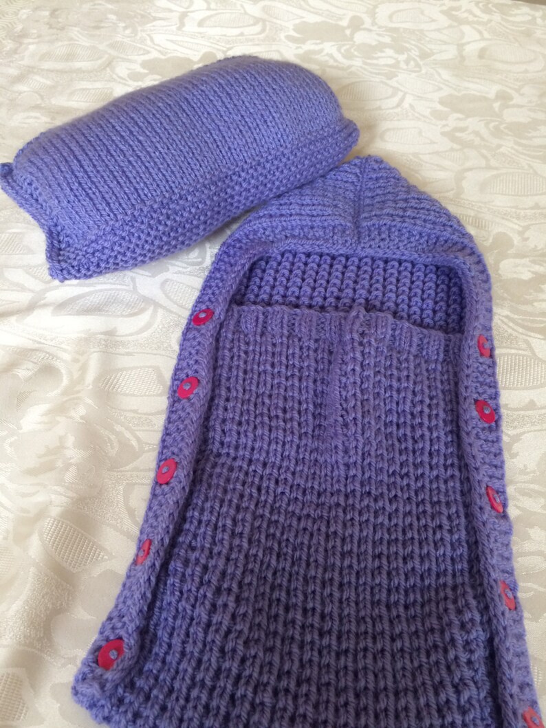 May include: A purple knitted baby sleeping bag with a hood and buttons down the side.