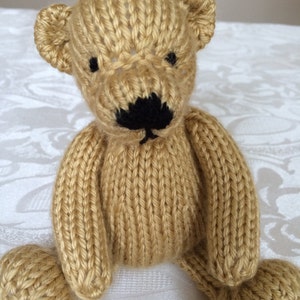 May include: A hand-knitted teddy bear with a brown body and black nose. The bear has a simple design and is made with a soft yarn.
