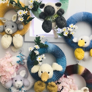 May include: A selection of handmade knitted wreaths, each with a different animal design. The wreaths are decorated with flowers and come in various colours, including yellow, blue, and green. The animals include a bunny, a sheep, and a duck.