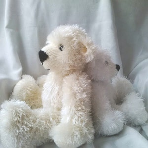 May include: Two white plush teddy bears sitting together. The bear on the left is looking to the side, while the bear on the right is looking straight ahead. Both bears have black eyes and noses.