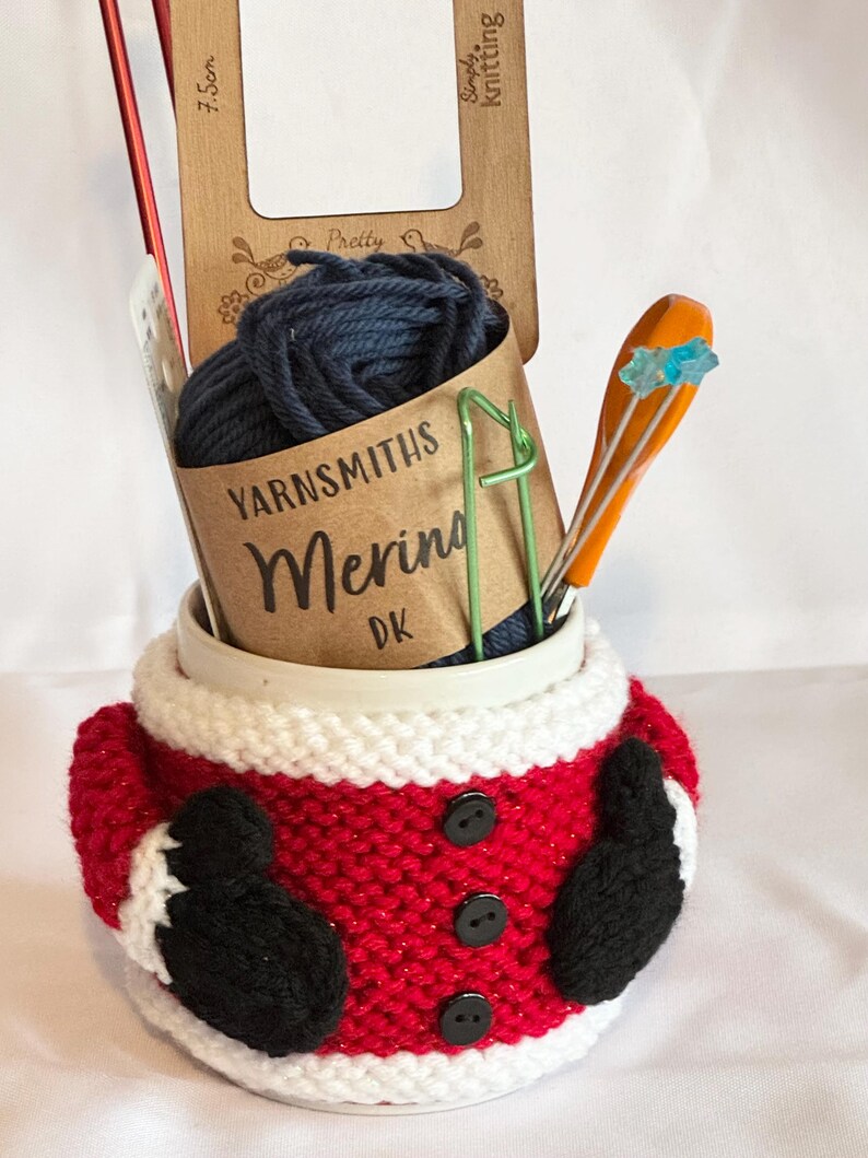 Puede incluir: Un kit de tejido navide&ntilde;o en un acogedor tema de Santa. El kit incluye lana azul marino, agujas de tejer, un calibrador de madera y un sujetador de puntadas. El acogedor es rojo con adornos blancos, botones negros y mitones negros.