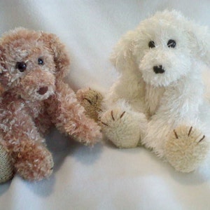 Pode incluir: Dois cães de pelúcia, um marrom e outro branco, sentados em uma superfície branca. Ambos os cães têm olhos pretos e narizes marrons.