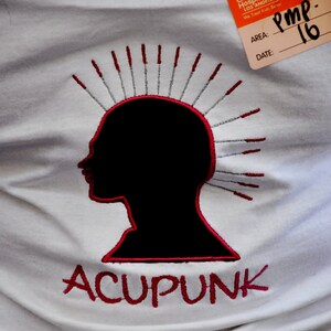 May include: White t-shirt featuring a black silhouette of a head with acupuncture needles and the word "ACUPUNK" in red. A Children's Hospital visitor badge is visible.