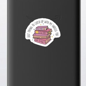 May include: A white sticker with a stack of pink books with the text "JUST TRYING TO CATCH UP WITH MY ENDLESS TBR" around the books. The book titles are "FATED MATES", "SLOW BURN", and "DARK ROMANCE".