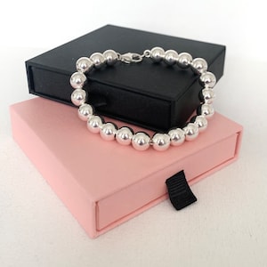 May include: A silver beaded bracelet with a clasp fastening, presented in a pink and black gift box.