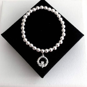 May include: A silver bracelet featuring a Celtic knot charm. The bracelet is made from small silver beads and has a simple design.