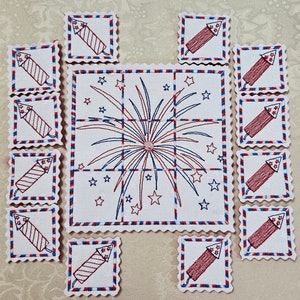 Puede incluir: Un conjunto de 12 cuadrados de tela con fuegos artificiales y petardos bordados en rojo, blanco y azul. Los cuadrados están diseñados para ser utilizados como un juego o un rompecabezas.