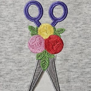 May include: Embroidered purple scissors with a bouquet of three flowers. The flowers are pink, red, and yellow.