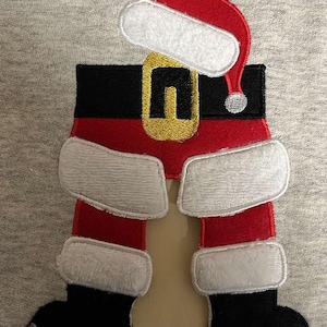 May include: A gray sweatshirt with an embroidered design of Santa Claus's legs and hat. The design features red, white, and black colors.