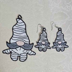 Op de afbeelding: Een set van drie geborduurde gnome-versieringen. De grootste gnome is een kerstversiering, terwijl de twee kleinere gnomes oorbellen zijn. Alle drie de gnomes zijn gekleed in wit-zwarte gestreepte outfits met zwarte baarden en roze neuzen.
