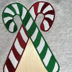 Puede incluir: Dos bastones de caramelo, uno verde y blanco, el otro rojo y blanco, están bordados sobre un fondo de tela gris.