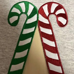 May include: Two candy canes, one green and white, the other red and white, are sewn onto a gray fabric background.