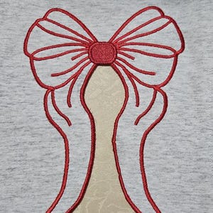 May include: Red embroidered bow with two wings on a gray fabric background.