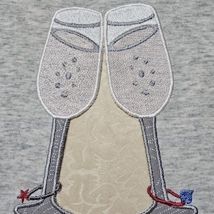 May include: Two embroidered champagne glasses with red and blue stars on the stems. The glasses are gray and white.