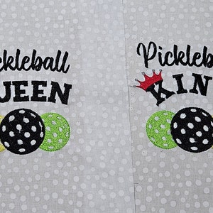 May include: Two embroidered towels with the words "Pickleball Queen" and "Pickleball King" with a crown above each word. Each towel has three embroidered pickleball paddles.