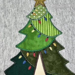 May include: A green felt Christmas tree with a gold star on top. The tree is decorated with colorful lights and has a brown felt trunk.