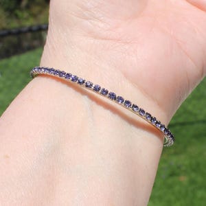 May include: A silver bangle bracelet with a row of small, purple gemstones.