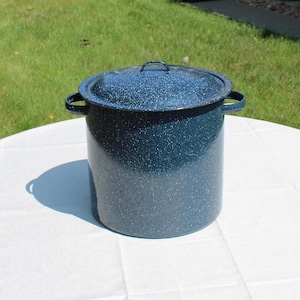 May include: A deep, cylindrical stockpot with a dark blue enamel finish featuring a white speckled pattern. The pot includes two side handles, a matching lid with a central handle, and a straight-sided design for large-capacity cooking tasks.