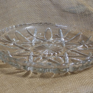May include: A clear glass serving dish with a scalloped edge and a starburst pattern. The dish has two handles on the sides.