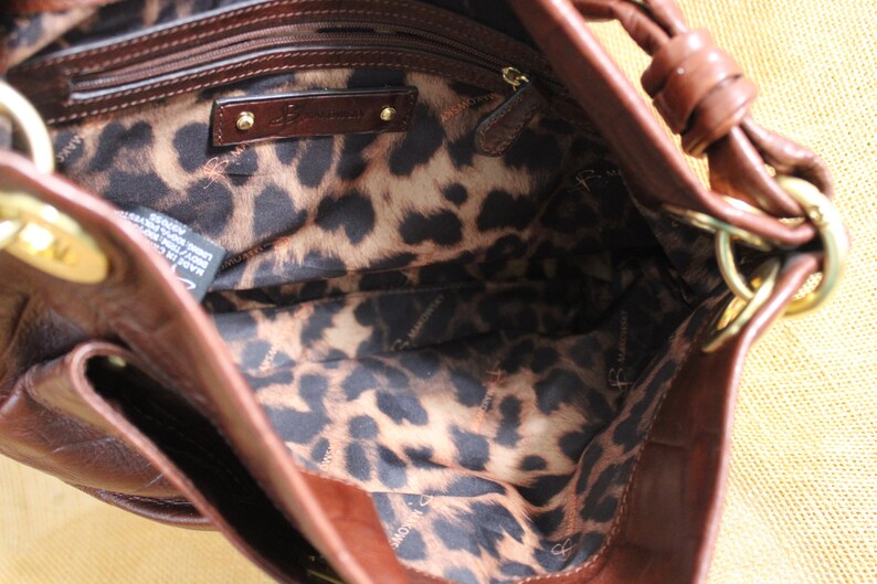 Op de afbeelding: Een bruine leren handtas met een luipaardprint voering. De tas heeft goudkleurige hardware en een handvat. De binnenvoering heeft een zwart-bruin luipaardpatroon. De tas is open en toont de binnenkant.