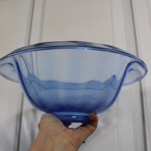 May include: A large, blue glass bowl with a wavy rim and a rounded base. The bowl is made of clear glass with a blue tint.