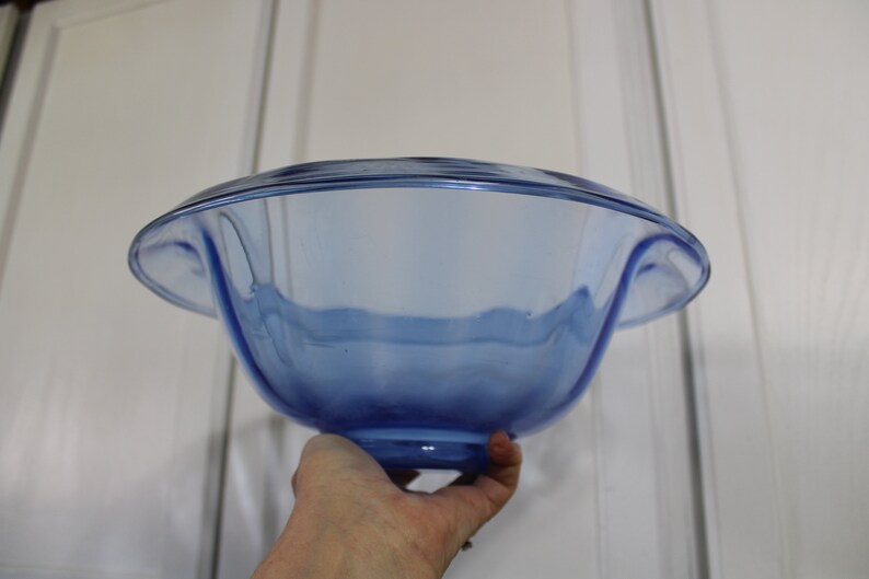 May include: A large, blue glass bowl with a wavy rim and a rounded base. The bowl is made of clear glass with a blue tint.