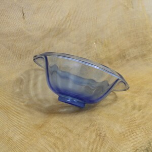 May include: A blue glass bowl with a wavy rim and a clear base. The bowl is sitting on a brown burlap surface.