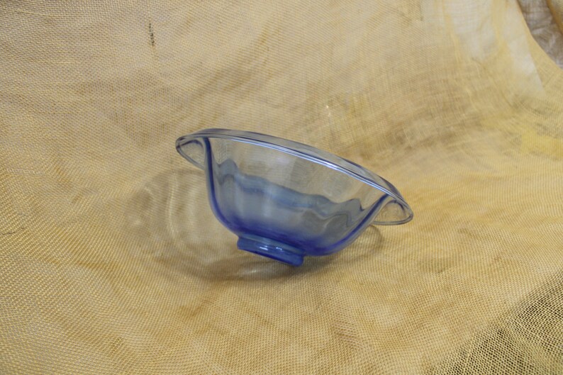 May include: A blue glass bowl with a wavy rim and a clear base. The bowl is sitting on a brown burlap surface.
