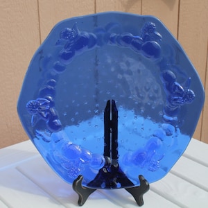 May include: A cobalt blue glass serving dish with a raised design of grapes and leaves around the rim. The dish has a textured surface with small bubbles throughout.