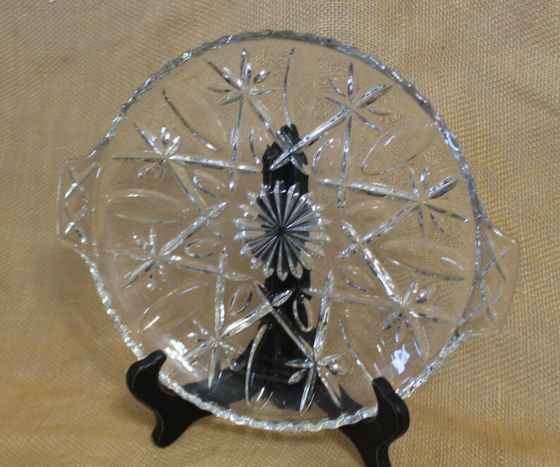 May include: A clear glass serving dish with a scalloped edge and a starburst pattern. The dish has two handles on the sides.
