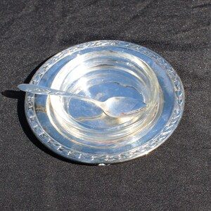 May include: A silver serving dish with a decorative rim and a small silver spoon inside.