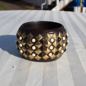 May include: A brown wooden bangle bracelet with a geometric pattern of gold and white studs.