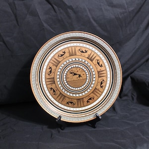 May include: A round, decorative plate with a black and gold geometric design. The center of the plate features a stylized image of a dolphin jumping over a wave.