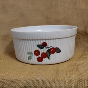 May include: White ceramic baking dish with a cherry design. The dish has a fluted rim and a white background with red cherries and green leaves.